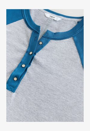 Grijze shirt met blauwe raglanmouwen, voorzien van een knoopsluiting in de henley-stijl en een soepele textuur. De knopen zijn rond met een lichte kleur.