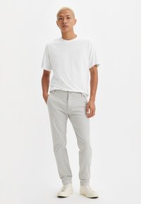 White cotton t-shirt paired with light gray slim-fit trousers. The individual wears white sneakers. Minimalistic design and neutral colors.