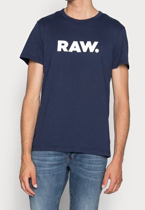 Marineblauwe katoenen t-shirt met een groot wit "RAW." logo op de voorkant. Korte mouwen en een ronde halslijn. Gladde textuur, casual pasvorm.