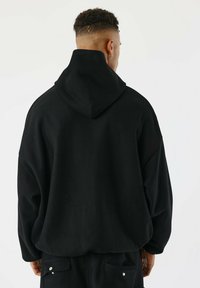 Sudadera negra de gran tamaño hecha de tela gruesa, con capucha de cuello alto, hombros caídos y un acabado texturizado para mayor profundidad.