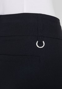 Pantalons noirs avec une texture lisse, dotés d'un anneau d'accent en argent et d'une poche arrière. La ceinture comprend des détails de couture pour la structure.