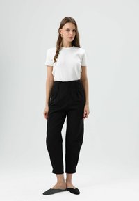 Wit shirt met korte mouwen gecombineerd met zwarte, hooggesneden broek met een nauwsluitende pasvorm en omgeslagen broekspijpen, aangevuld met zwarte instapschoenen.