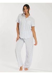 Ljusblå pyjamasset som består av kortärmad skjorta med knappar och vågiga kanter, samt långa byxor med prickigt mönster.