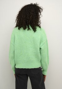 Lichtgroene gebreide trui met een lose fit, geribbelde zoom en licht oversized mouwen, gecombineerd met donkergrijze jeans.