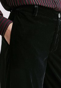 Mustad korgloomused, millel on sile tekstuur ja õrn sära. Omavad esipaneeli taskut ja nööpklappi, stiilitud triibulise särgiga.