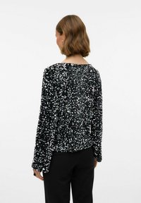 Črn dolg rokav s povrhnjico iz bleščic, z okroglo ovratnico in ohlapnim krojem, v kombinaciji s črnimi hlačami. Prikazana je zadnja stran.