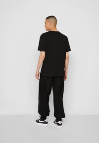 Svart bomull T-skjorte med korte ermer, avslappet passform, kombinert med svarte cargo-bukser med cargo-lommer, antrukket med svart-hvite sneakers.