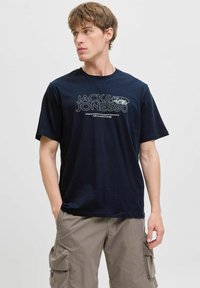 Tamsiai mėlynas medvilnės marškinėliai su grafika, kurioje yra "JACK & JONES" ir šūkis. Trumpi rankoviai, apvalus kaklas ir laisvas kirpimas.