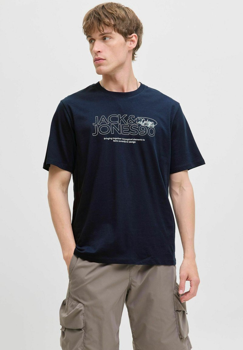 Tamsiai mėlynas medvilnės marškinėliai su grafika, kurioje yra "JACK & JONES" ir šūkis. Trumpi rankoviai, apvalus kaklas ir laisvas kirpimas.
