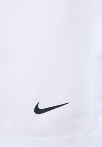 Biely športový tričko s textúrovanou tkaninou; má malú čiernu Nike swoosh logo na prednej strane. Jednoduchý, minimalistický dizajn.