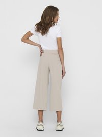 Beige vide bukser med elastisk talje, parret med en hvid tætsiddende t-shirt og afslappede sneakers, set fra ryggen.