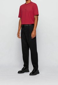 Bordový tričko s krátkým rukávem a černým logem, kombinované s černými kalhotami na míru a černými šněrovacími botami, s elegantním designem.