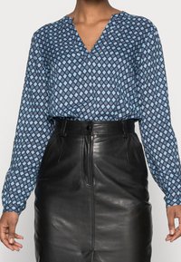 Blue geometric patterned blouse with long sleeves, V-neckline; paired with a high-waisted black leather skirt, smooth texture.