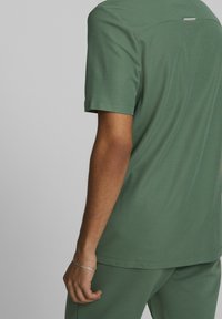 Grön kortärmad skjorta med en mjuk textur, med en rundad axelsöm och liten horisontell etikett på baksidan.