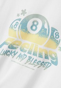 Camiseta blanca de algodón con un diseño gráfico en colores azul y amarillo. El texto dice "Sintiendo que tengo suerte y bendiciones", con un efecto desgastado.