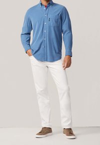 Lichtblauw overhemd met knopen, voorzien van een borstzak, witte broek en bruine sneakers. Het overhemd heeft lange mouwen en een kraagdesign.