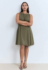 Rochie fără mâneci, de culoare verde măsliniu, cu un croi lejer și fustă evazată. Fabricată dintr-un material moale, având un design minimalist și fără modele vizibile.