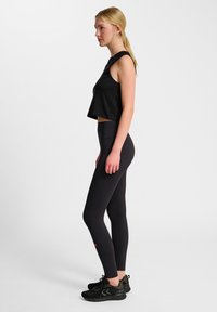 Zwarte cropped tanktop en zwarte high-waisted legging met textuuraccent, gecombineerd met zwarte sportschoenen.