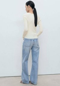 Aansluitende crèmekleurige ribgebreide trui gecombineerd met lichtblauwe high-waisted wijde jeans, met achterzakken en een relaxte pasvorm.