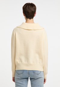 Cremfarbener Strickpullover mit großem umgeschlagenem Kragen, gerippten Bündchen und Saum, der eine weiche Textur und eine lässige Passform aufweist.