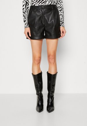 Pantalones cortos de cuero negro con un ajuste entallado, que presentan una textura suave y un dobladillo enrollado. Combinados con botas negras brillantes hasta la rodilla.