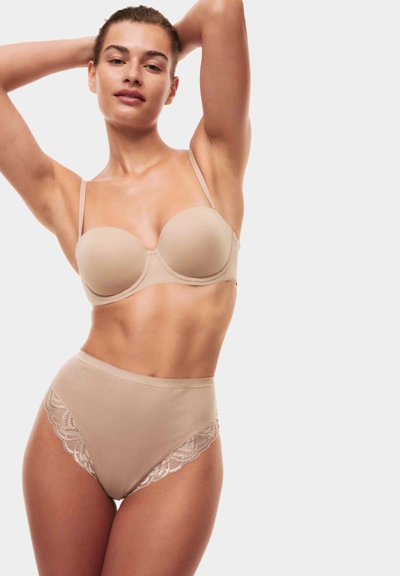Beige bh med släta kupor och justerbara axelband, parat med högmidjade beige trosor med spetsdetaljer på sidorna.