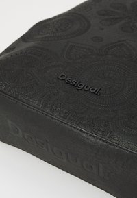 Zwarte, gestructureerde tas met reliëf cirkelpatronen en subtiele branding. Heeft een soepele, lederen afwerking en een rechthoekige vorm.