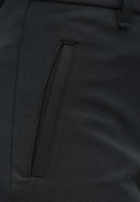 Pantalon noir à texture lisse, doté d'une poche latérale à ouverture incurvée et d'un détail de couture discrète.