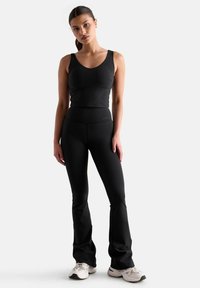 Czarny sportowy top na ramiączkach i legginsy rozkloszowane wykonane z elastycznego materiału, charakteryzujące się gładką teksturą i dopasowanym krojem. Akcentowane minimalnym logo.