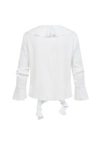 Blusa blanca de manga larga con puños con volantes, un cuello con volantes y dos detalles de lazos en la parte delantera, vista desde atrás sobre un fondo liso.