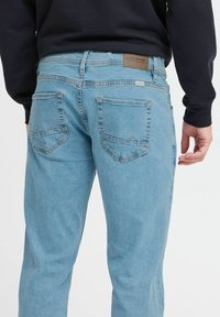 Jeans de denim azul claro con un corte regular, que cuentan con dos bolsillos traseros y costuras en contraste, diseñados con una etiqueta de cuero marrón en la cinturilla.