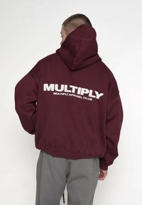 Bluza z kapturem w kolorze bordowym o luźnym kroju. Na plecach dużymi białymi literami napis "MULTIPLY" oraz "MULTIPLY APPAREL CLUB".