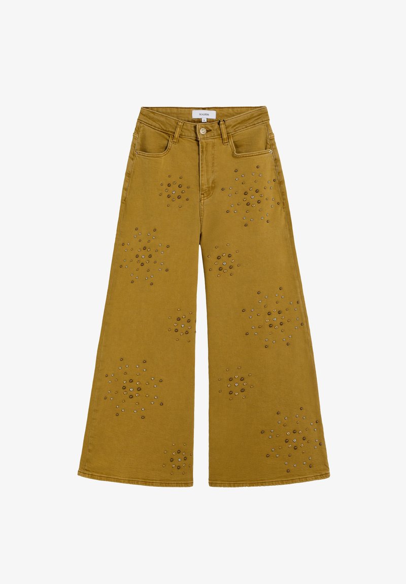 Pantalones de pierna ancha en denim amarillo mostaza con adornos de tachuelas metálicas circulares dispuestos en patrones de flores en la parte delantera.
