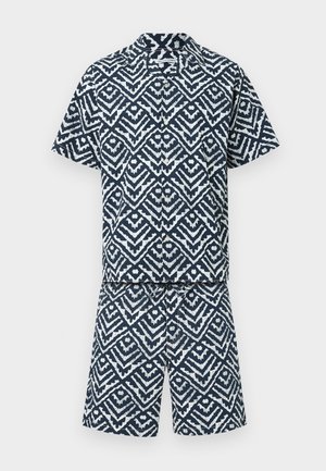 Passendes kurzärmeliges Hemd zum Knöpfen und Shorts mit marineblauem und weißem geometrischem Tribal-Muster auf einfarbigem Hintergrund.