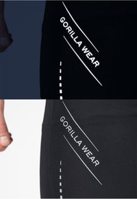 Zwarte sportbroek met reflecterende witte opdruk met de tekst "GORILLA WEAR." Heeft een gladde textuur met gebogen en onderbroken lijnaccenten.