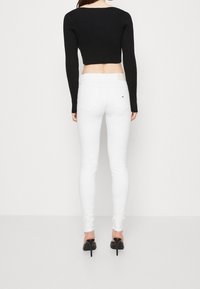 Top corto de canalé negro combinado con jeans skinny blancos. Los jeans cuentan con bolsillos traseros y un pequeño detalle del logo cerca de la cintura. Zapatos de tacón alto.