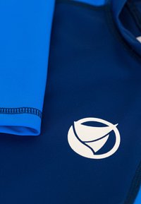 Muta a maniche lunghe in blu e blu scuro, con una texture liscia, design aderente e un logo bianco circolare sul petto.