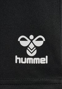 Tessuto nero con una finitura testurizzata, caratterizzato da un prominente logo bianco "hummel" con un design stilizzato di un'ape sopra il testo.
