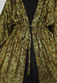 Zielony rajstopy z wzorem paisley, z zaznaczoną talią, wykonany z lekkiego materiału, z żółtymi akcentami floralnymi i dekoltem w kształcie litery V.