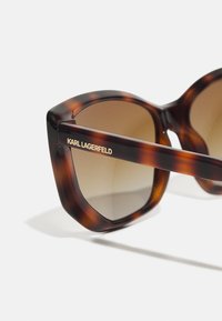 Skilpadde-solbriller med vinklet design, brune gradientlinser, og subtil gulltekst som leser "KARL LAGERFELD" på stangen.