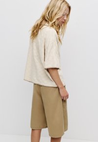 Top bej texturat cu mâneci scurte și cu o margine rotunjită, asociat cu pantaloni scurți kaki până la genunchi. Design simplu cu detalii de cusătură subtile.