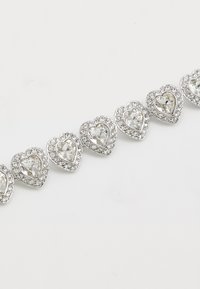 Bracelet en ton argenté avec des maillons en forme de cœur ornés de pierres claires facettées, entourées de plus petits strass, créant un effet scintillant.
