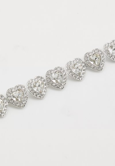 Bracelet en ton argenté avec des maillons en forme de cœur ornés de pierres claires facettées, entourées de plus petits strass, créant un effet scintillant.