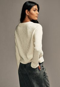 Lichtcrème gebreide trui met lange mouwen, gecombineerd met hoge donkerdenim jeans, die casual, ontspannen styling laat zien.