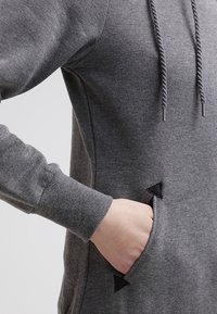 Harmaa huppari, jossa on kengurutasku mustilla kolmiokuvioilla ja teksturoidut hihansuut. Materiaali vaikuttaa pehmeältä ja hieman harjatulta.