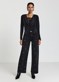 Black draped long-sleeve top with lace detail, paired with wide-leg black jeans featuring silver grommet accents throughout. Black heeled boots.