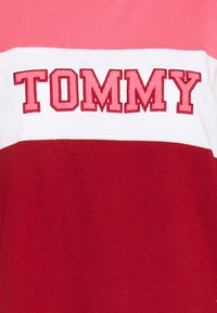 T-shirt i bomull med horisontella färgblock i ljusrosa, vitt och rött, med "TOMMY" broderat i fet stil i röda bokstäver.