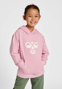 Rosa Kapuzenpullover mit einem weißen Grafikdesign, das ein symmetrisches Muster zeigt. Weicher Stoff, Kängurutasche und Kapuze mit Kordelzug. Grüne Hose.