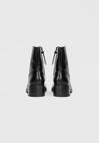 Botas de cuero negro hasta el tobillo con una textura suave, cremalleras traseras y un tacón bloque modesto. Detalle del logo en el tacón para la marca.