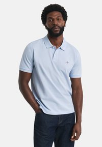 Jasnoniebieska koszulka polo z krótkim rękawem i klasycznym kołnierzykiem, z małym logo na klatce piersiowej oraz miękkim, teksturowanym materiałem bawełnianym.